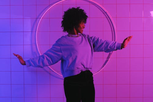 Stylish black woman standing with raised arms in room with neon lights in room with neon lights