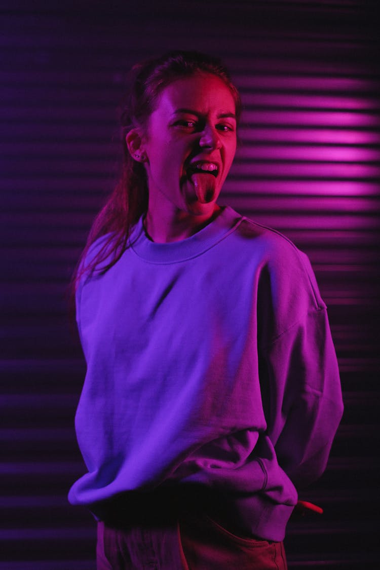 Female Showing Tongue In Dark Room With Neon Illumination