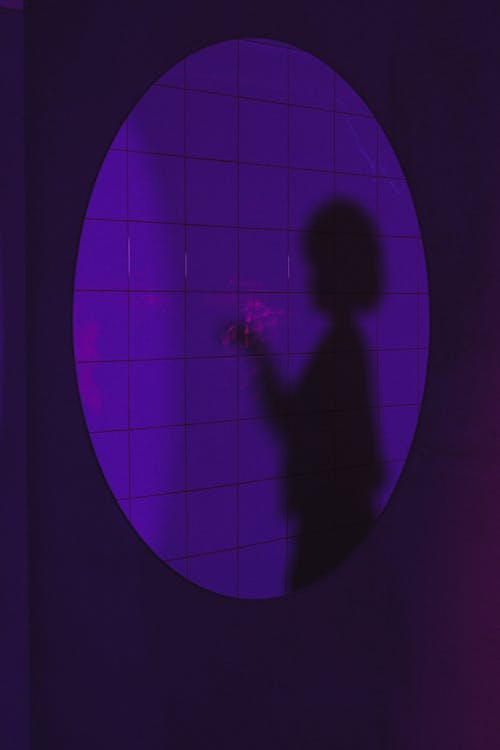 Free Shadow of female with hairstyle standing with raised arm near wall in room with neon lights Stock Photo