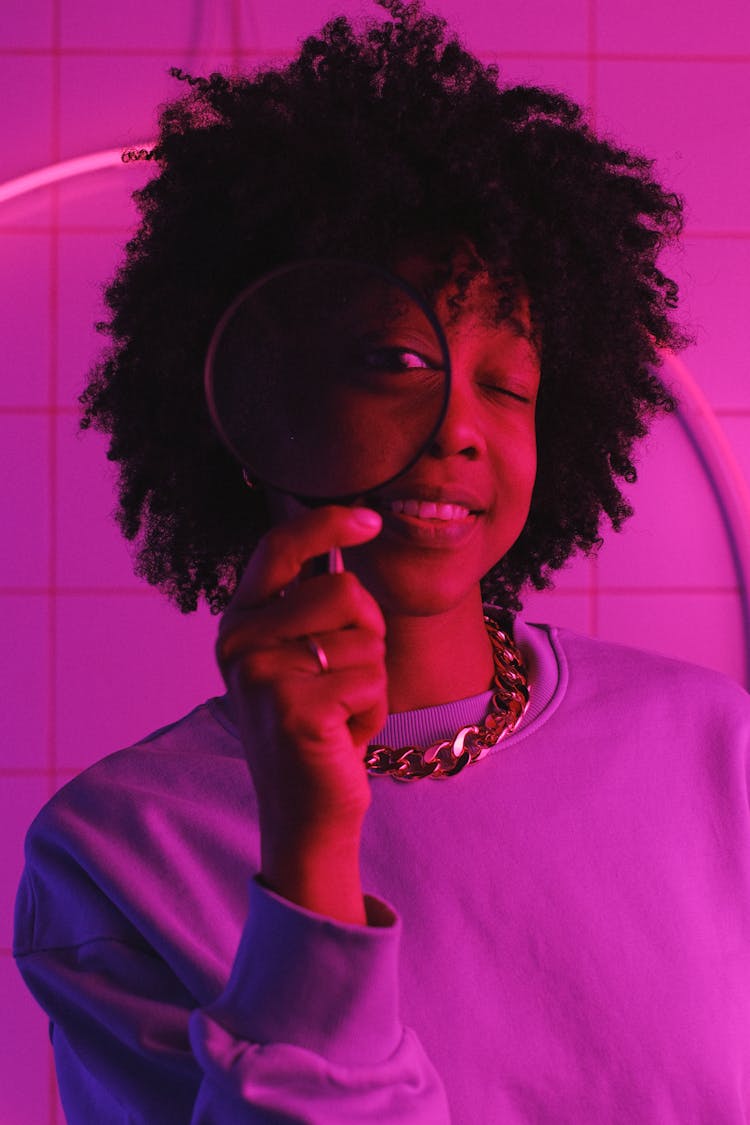 Smiling Black Woman Standing With Magnifier In Room With Neon Lights