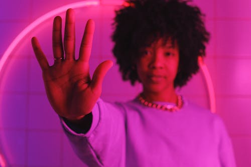 Serious black woman standing with raised arm in room with pink illumination