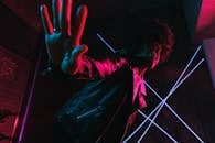 Low angle of trendy black female adolescent leaning forward while demonstrating control gesture and looking at camera against lamps at night