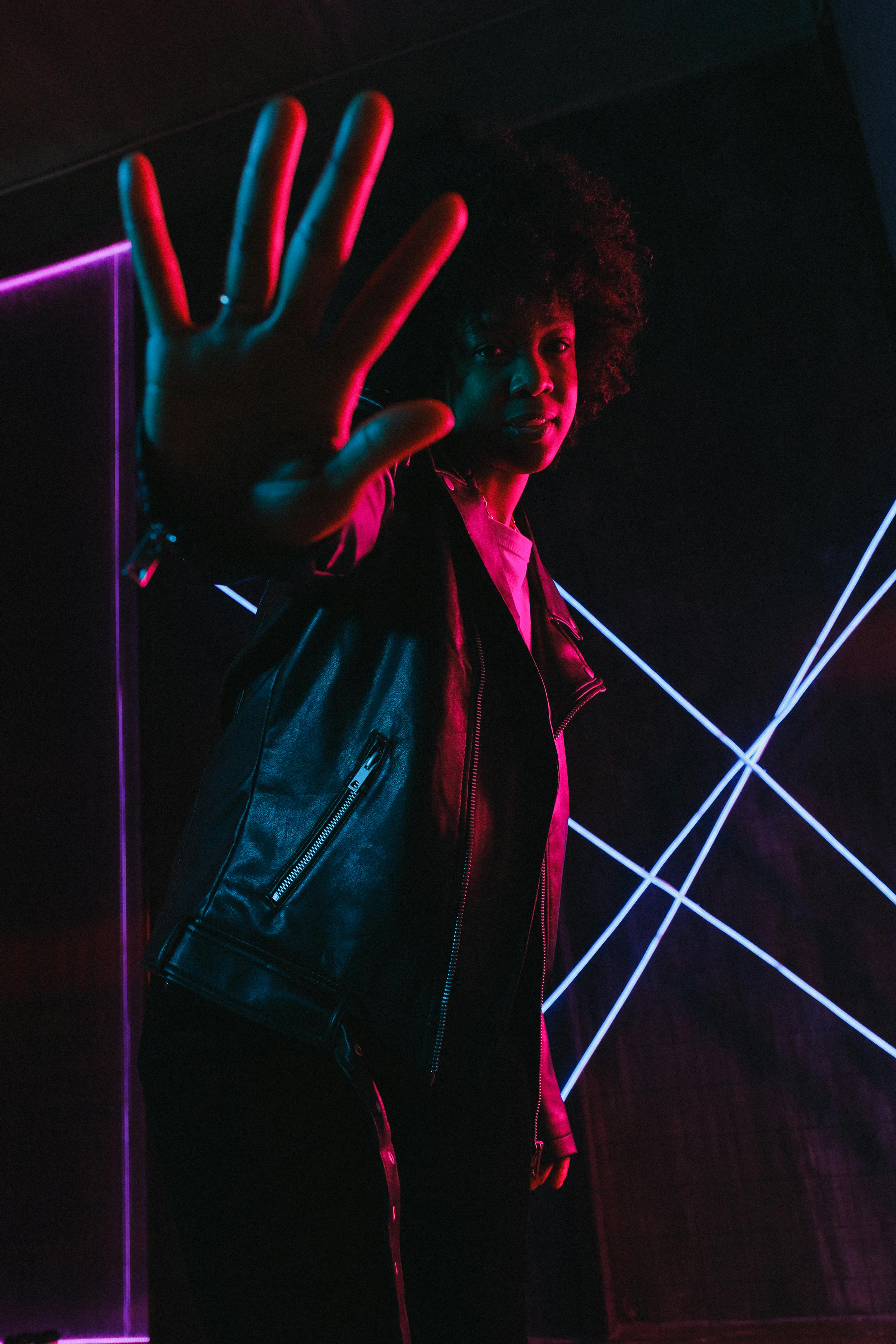 black teen showing stop gesture in neon light at dusk