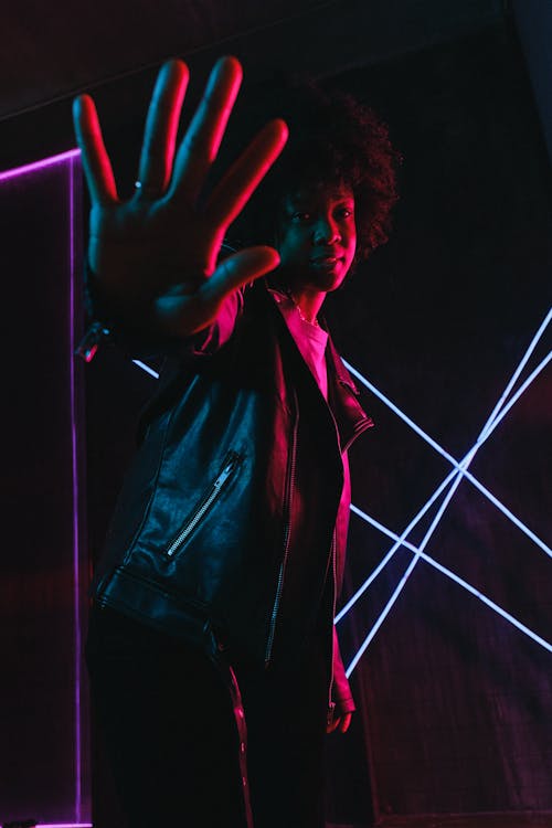 Black teen showing stop gesture in neon light at dusk