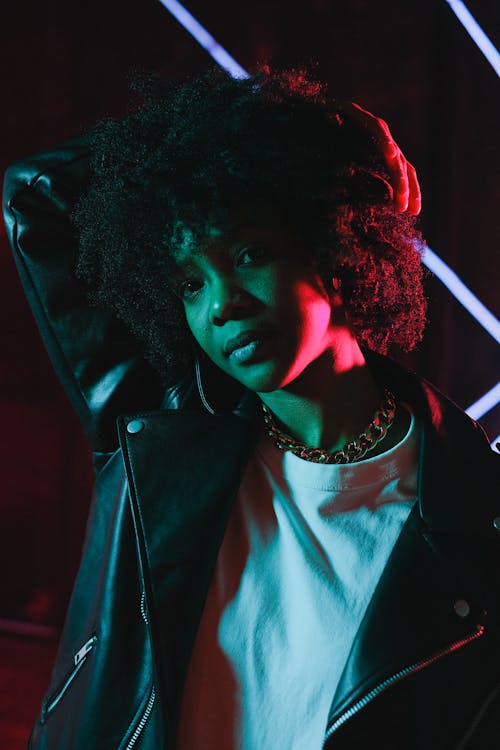 Stylish black woman standing in dark studio in neon light