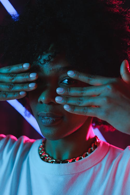 Attractive black woman covering eyes with hands in dark studio
