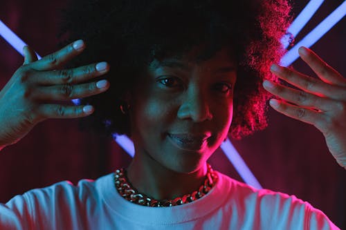 Cheerful black woman raising hands near face in neon illumination