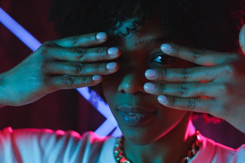 Crop black woman covering eyes with hands in neon illumination