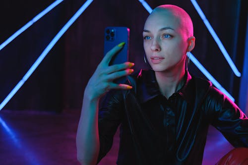 Young Bald woman using photos on smartphone in neon studio