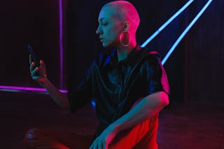 Thoughtful bald woman using smartphone in neon studio