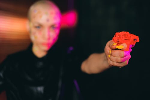 Eccentric bald woman pointing toy gun in dark studio