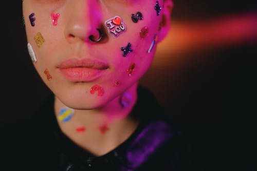 Crop woman with multicolored stickers on face in dark studio