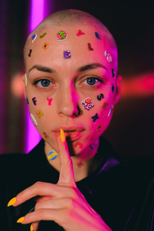 Bald woman with stickers on face showing shush sign