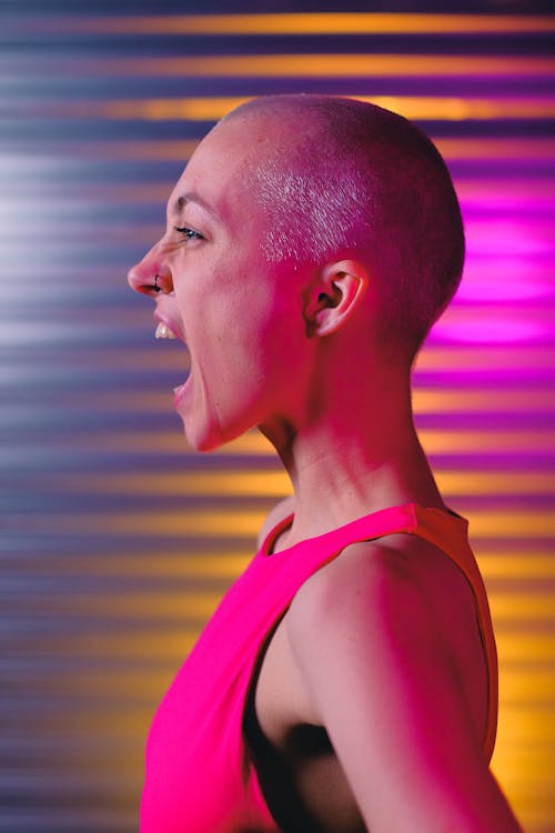 Side view eccentric bald female in pink top yelling loud in colorful studio