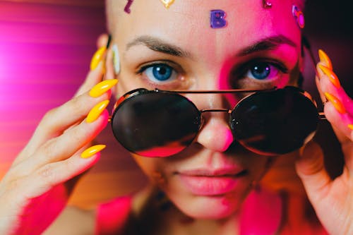 Crop bald woman with sticker on face lowering sunglasses