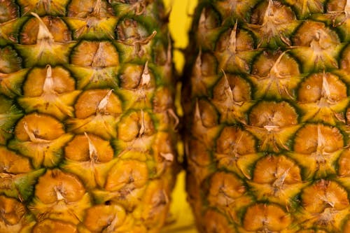 Closeup details of fresh whole pineapples with brown textured skin for healthy diet placed on yellow background in light studio