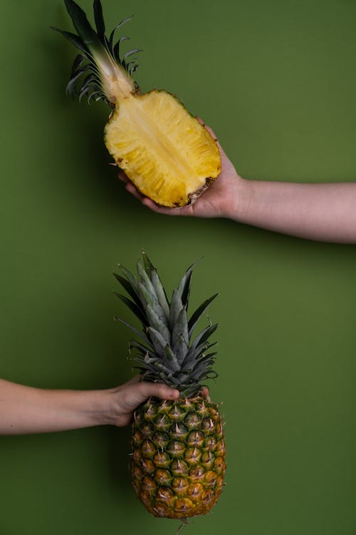 Unrecognizable people with whole and halved pineapple