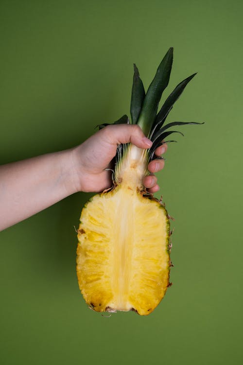 Ripe cut pineapple with juicy pulp demonstrated by crop anonymous person on green background
