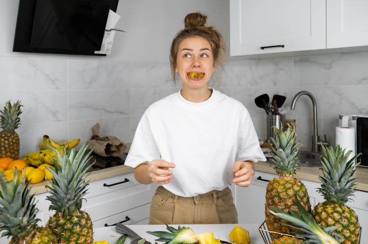 Woman With Slice Of Pineapple In Mouth In Kitchen