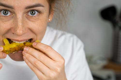 Free Cheerful female with freckles looking at camera and biting fresh pineapple at home Stock Photo