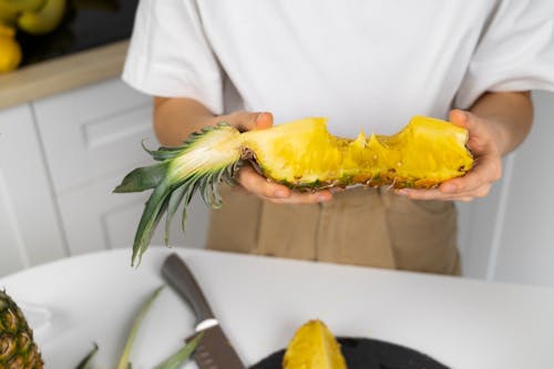 Crop unrecognizable person demonstrating delicious fresh pineapple piece with juicy flesh above table in house