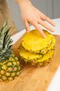 Crop unrecognizable person touching delicious fresh pineapple circles on wooden chopping board in house kitchen