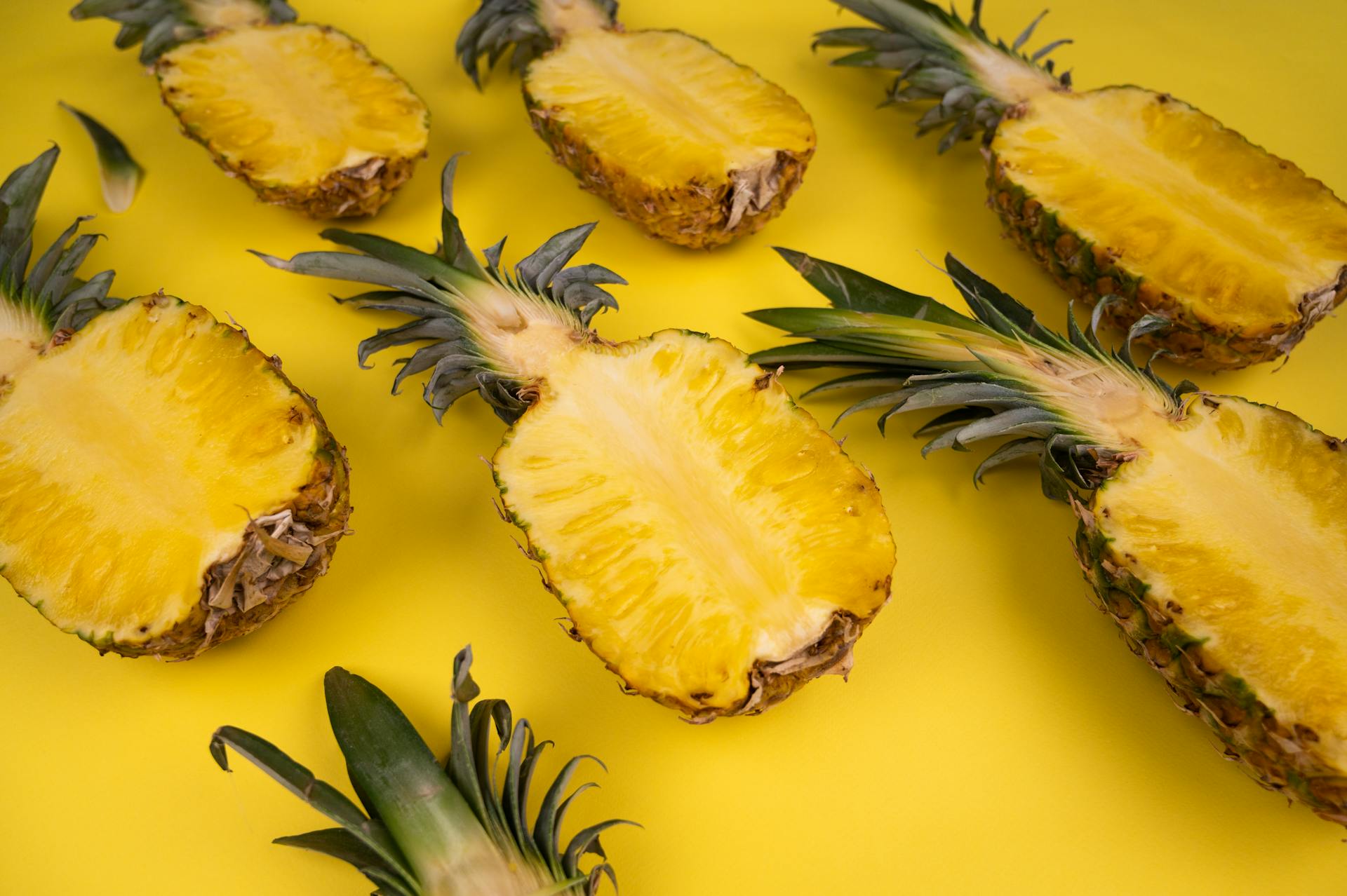 From above of fresh cut pineapples with sweet flesh and green leaves on yellow background