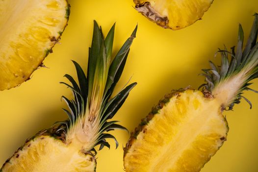 Overhead view of yummy cut pineapples with sweet flesh and wavy leaves on yellow background