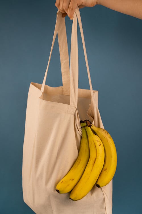 Free Crop person with bunch of fresh bananas in eco bag Stock Photo