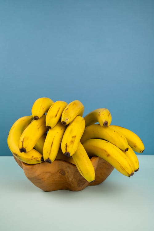 Bundle of tasty ripe bananas with spots on yellow peel in bowl on two color background