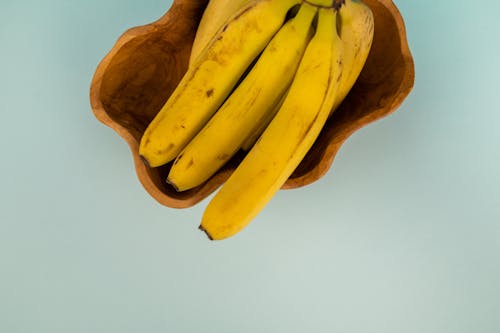 Top view of bunch of fresh bananas with blots on smooth yellow peel in curved bowl on light background