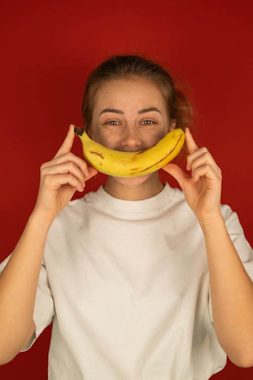 Free Smiling woman covering mouth with fresh banana Stock Photo