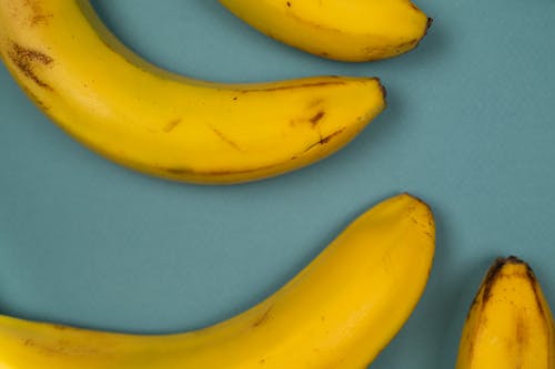 Free From above of tasty ripe bananas with blots on smooth yellow peel on blue background Stock Photo