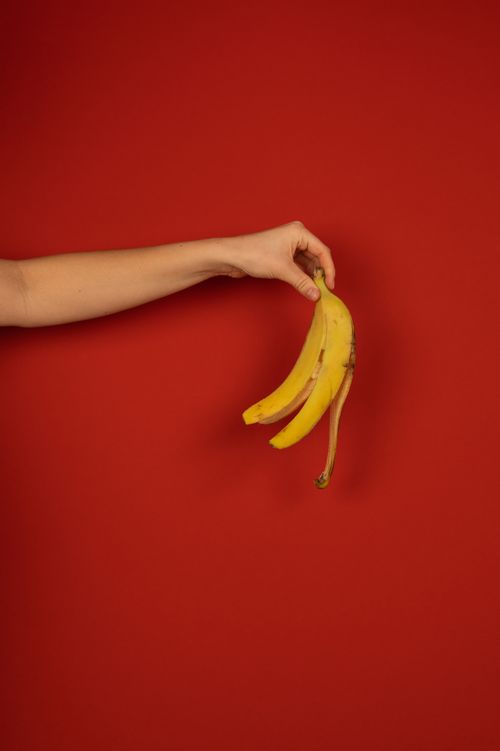 Free Crop unrecognizable person with outstretched arm demonstrating yellow peel of fresh banana on red background Stock Photo