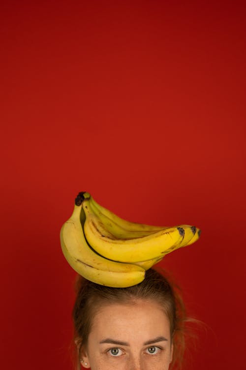 Crop woman with bunch of ripe bananas on head