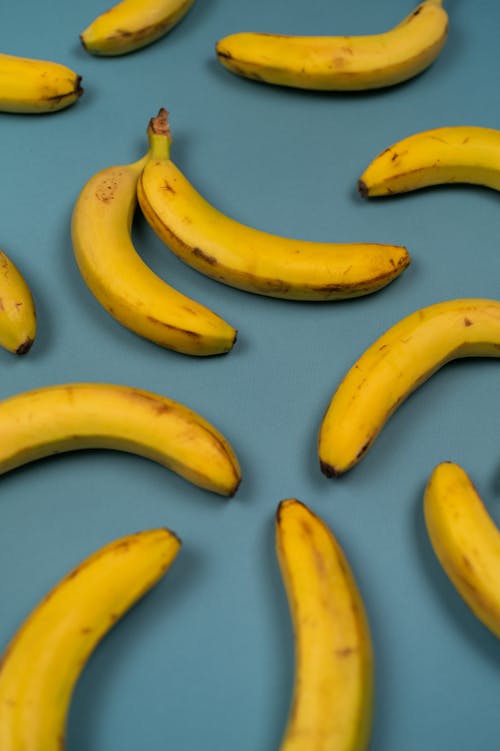 High angle of delicious fresh bananas with stems and blots on smooth peel on blue background