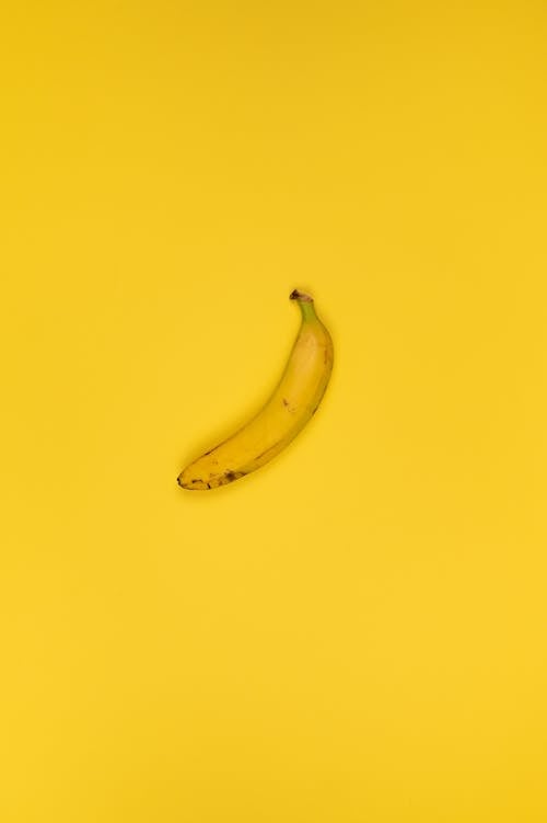 Top view of delicious ripe banana with stem and blots on peel on bright yellow background