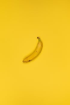 Top view of delicious ripe banana with stem and blots on peel on bright yellow background