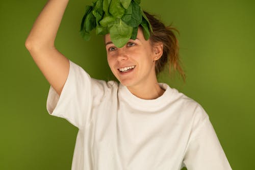 Smiling woman with spinach leaves on green background