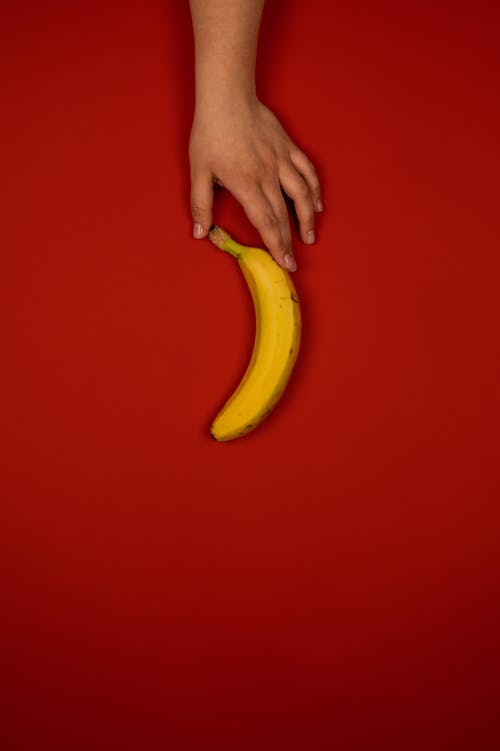 Faceless person with tasty ripe banana on red background