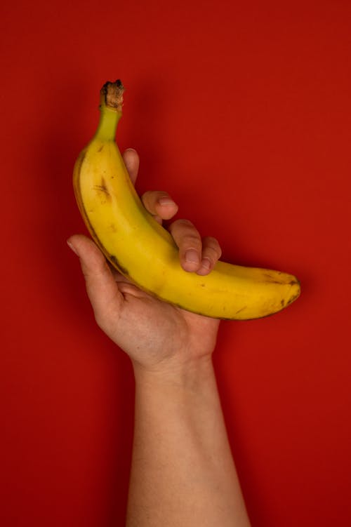 Faceless person showing fresh banana on red background
