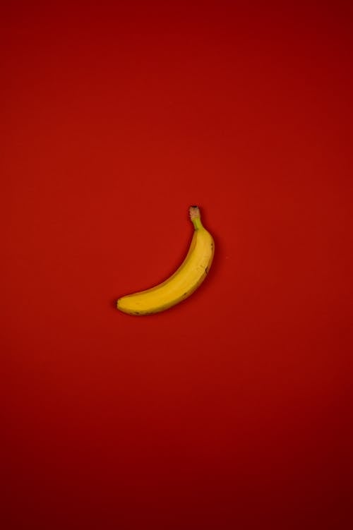Top view of delicious fresh banana with wavy stalk and yellow peel on red background