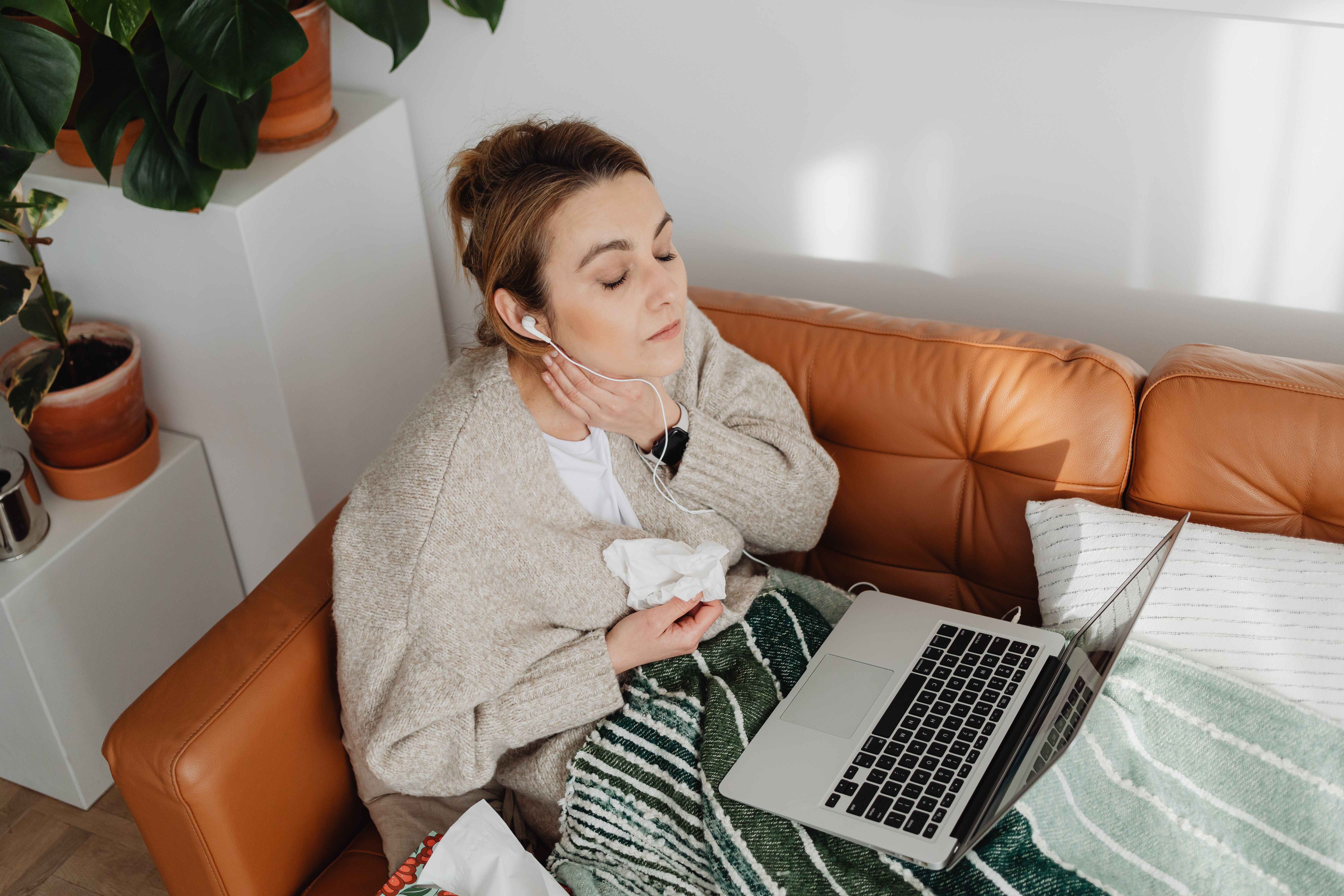 Woman relaxing with earphones on a cozy couch. Indoor scene with laptop and plants.