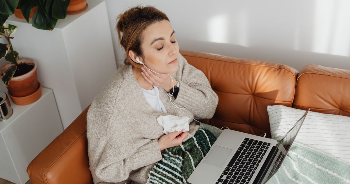 Woman relaxing with earphones on a cozy couch. Indoor scene with laptop and plants.