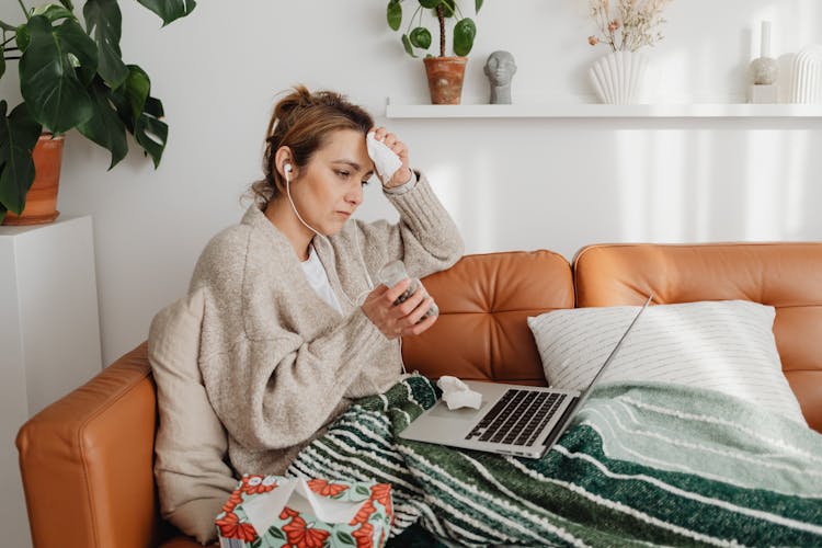 Sick Woman Sitting On A Couch Using Laptop 