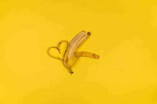 Top view of ripe heart shaped banana peel with spots and stalk on yellow background