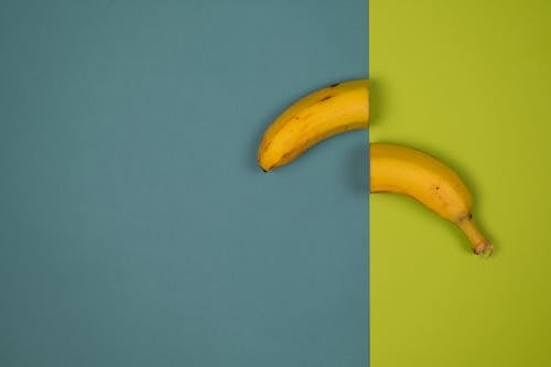 Overhead view of delicious cut fresh banana with stem and spots on peel on smooth surface