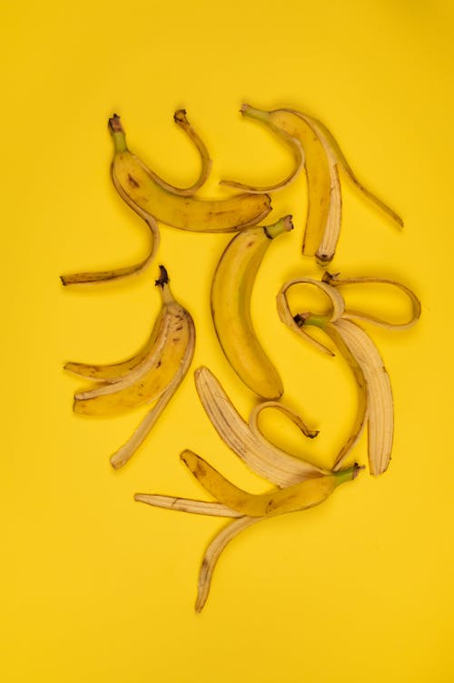 Delicious ripe banana among peel on yellow background