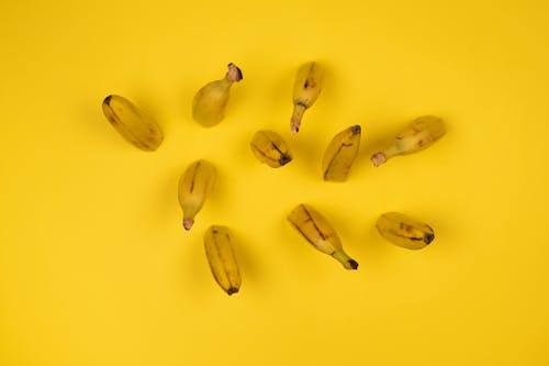 Overhead view of delicious ripe banana halves with stems and blots on peel on yellow background