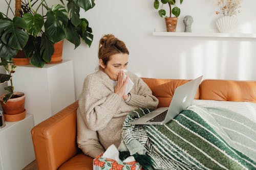 Free Woman Wiping Her Nose While Using a Laptop on Sofa  Stock Photo